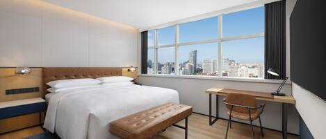 Una habitación de hotel moderna con una cama grande, un escritorio y vistas al horizonte de la ciudad.