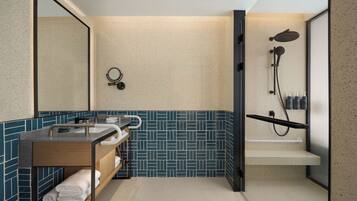 A modern bathroom with a freestanding sink, a mirror, a towel rack, a shower enclosure, and a tiled backsplash.