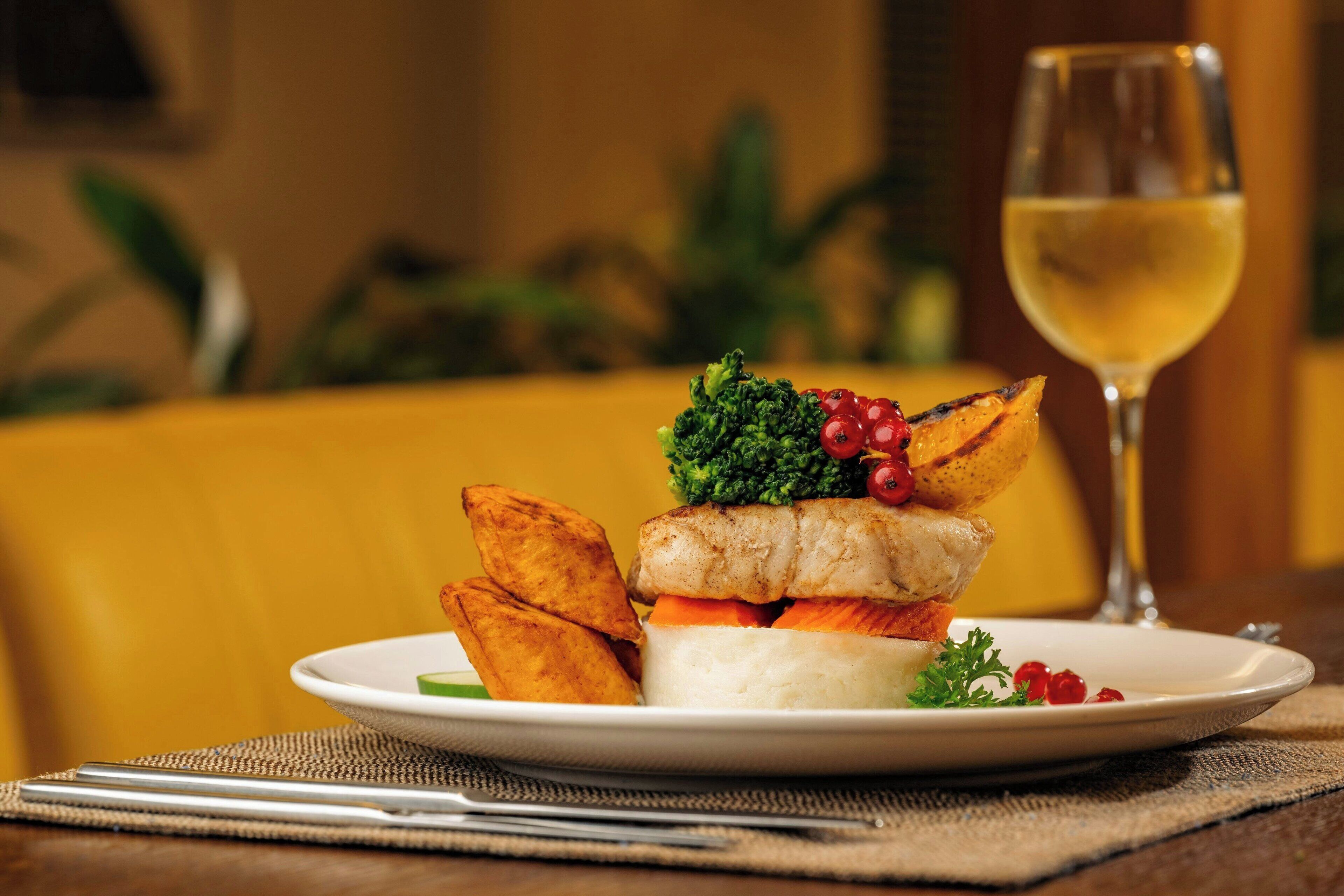 A plate of food with a glass of white wine on a table.