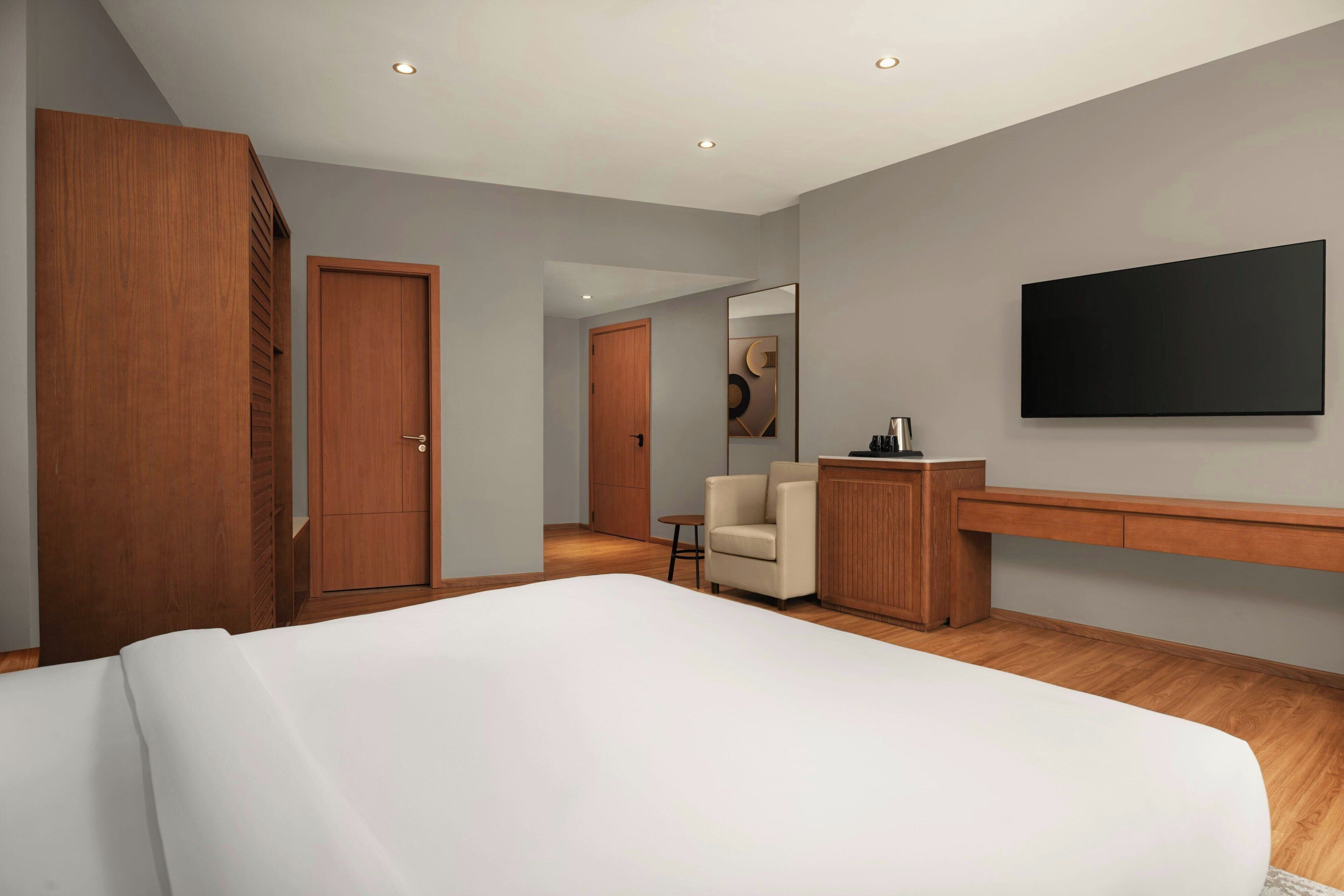 A modern hotel room with a large bed, a desk, a chair, and a TV mounted on the wall.