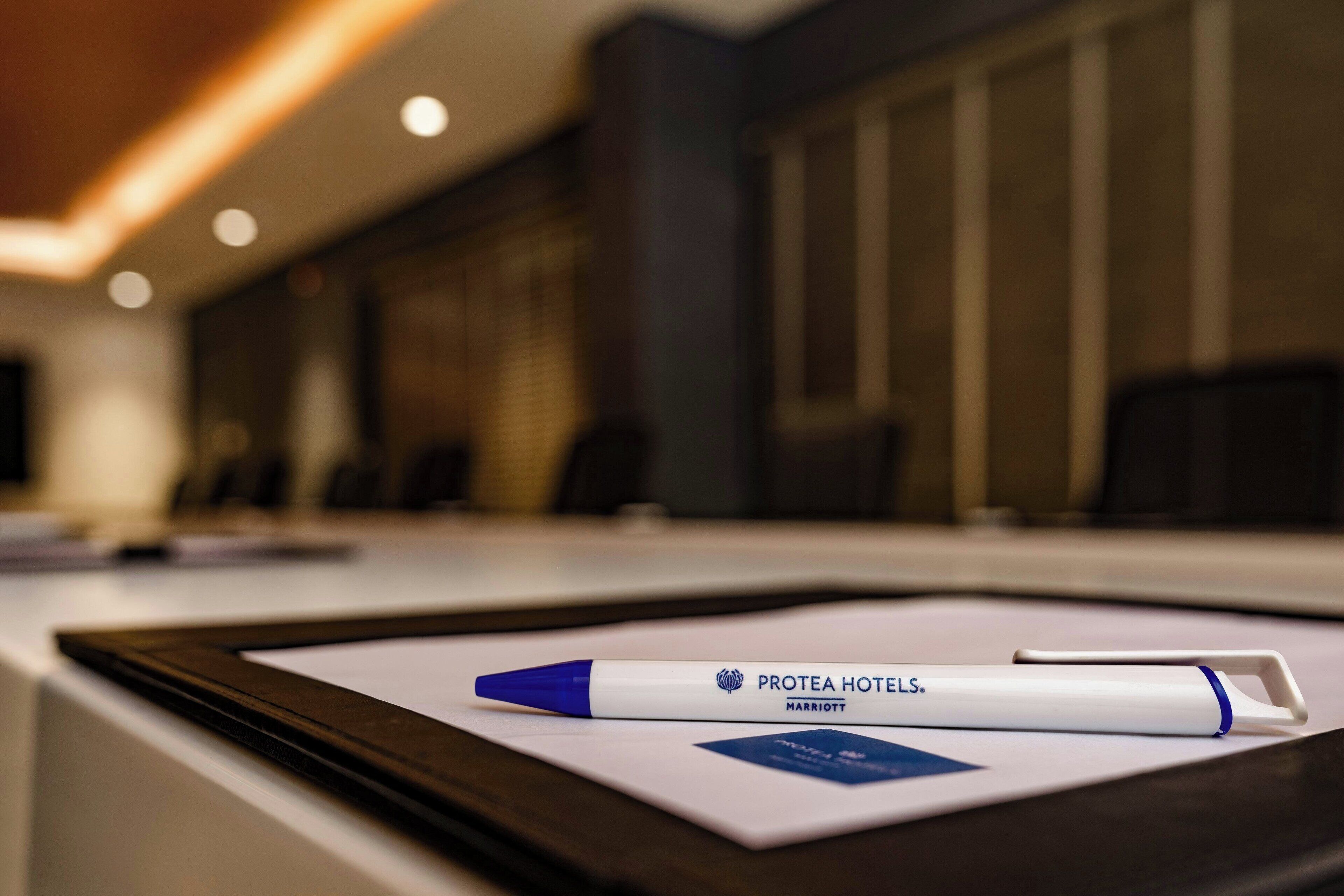 A Protea Hotels Marriott pen on a table with a framed picture and a small blue card.