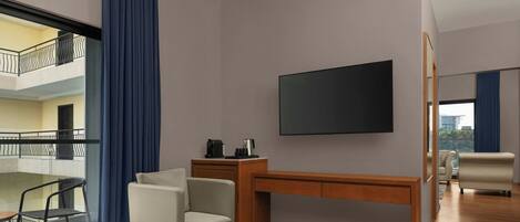 Habitación de hotel con cama, escritorio, silla, una mesita, televisor y balcón con barandilla.
