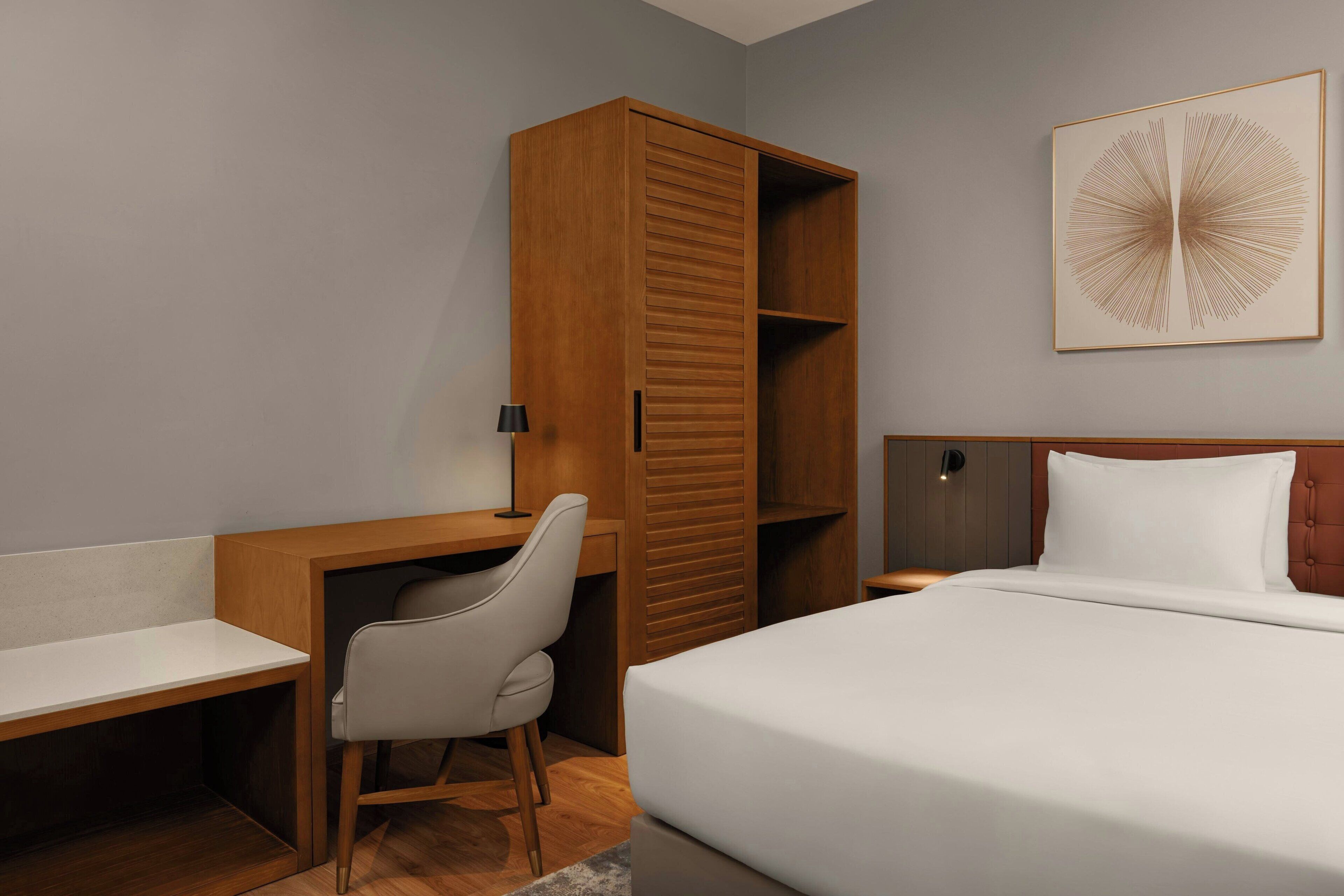 Une chambre à coucher comprenant un lit, un bureau, une chaise, une armoire et une œuvre d’art accrochée au mur.