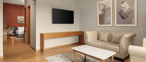 A modern living room with a wooden bench, a white coffee table, a beige sofa, and a flat-screen TV mounted on the wall.