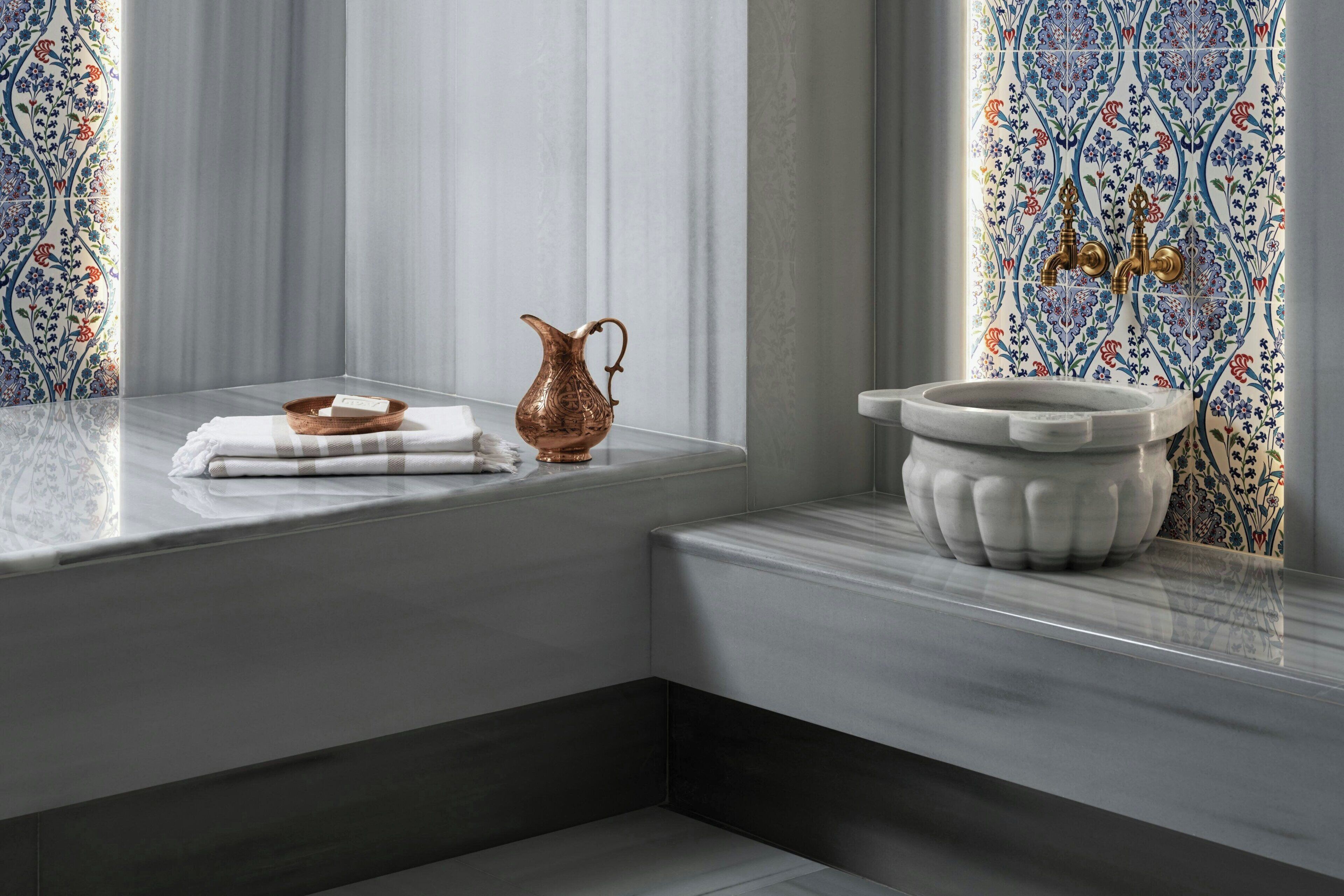 A bathroom with a marble sink, a copper pitcher, and a decorative tile backsplash.