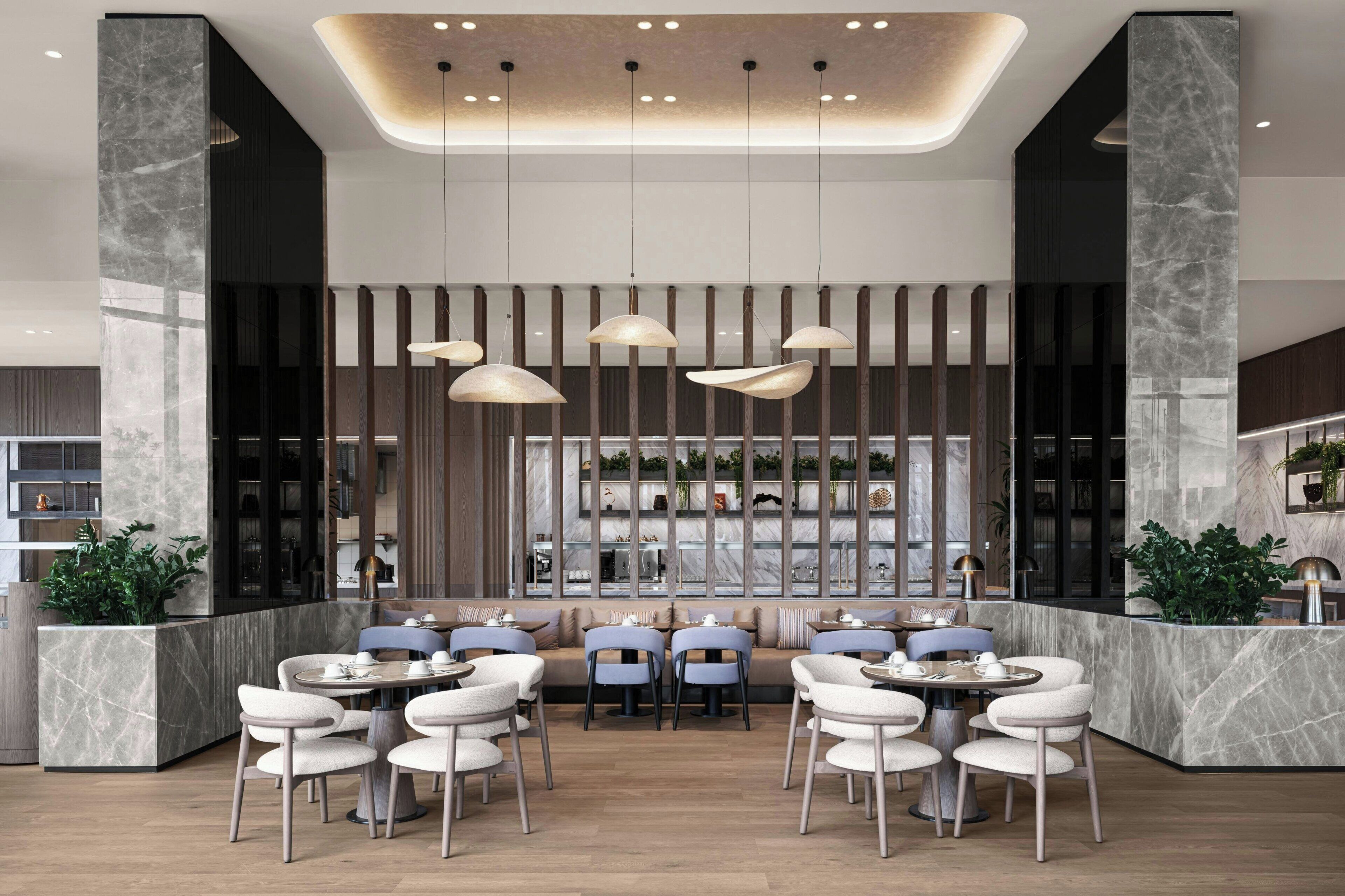 Un comedor moderno con columnas de mármol, iluminación colgante y una distribución central de mesas y sillas.