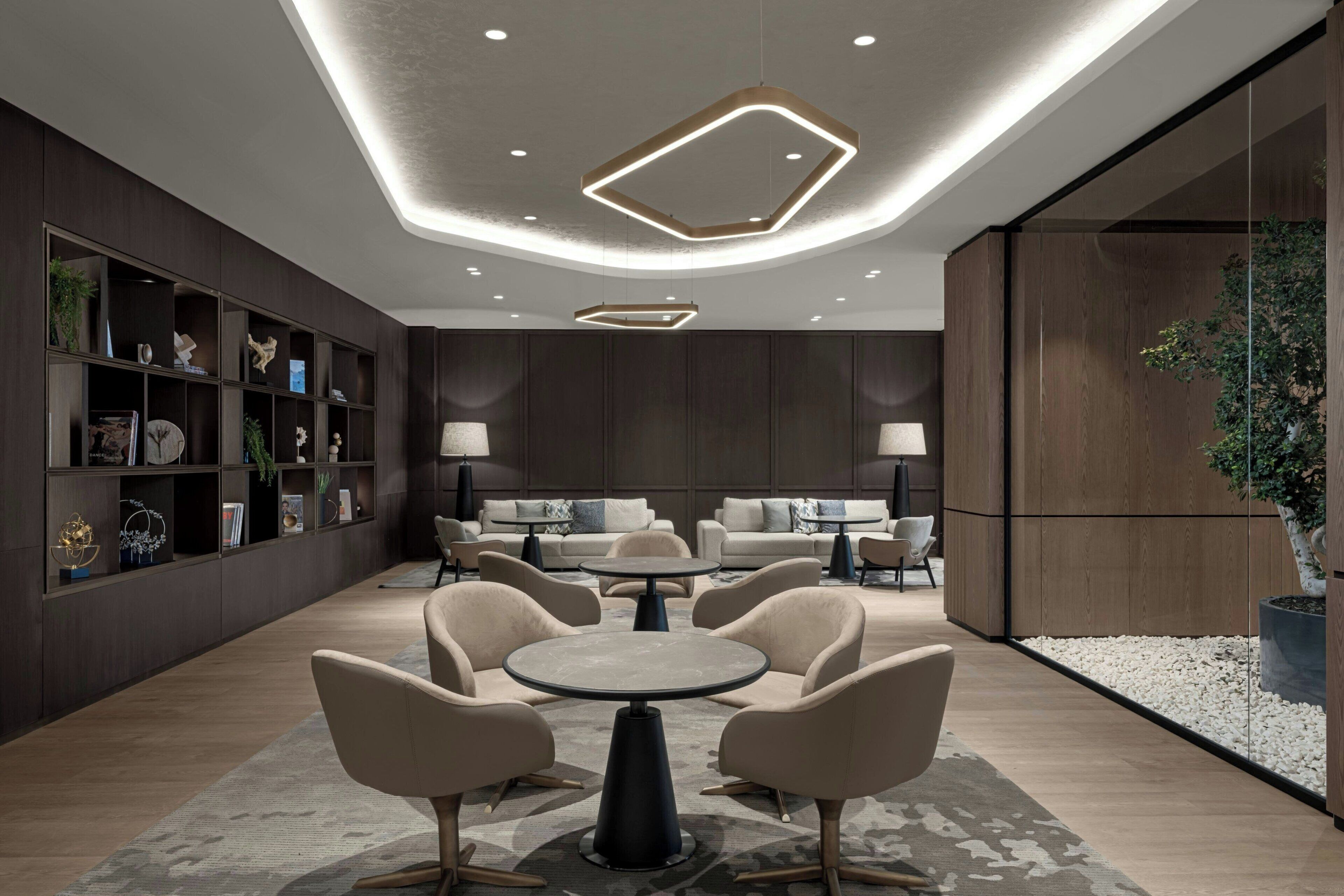 Een modern interieur met een ronde centrale tafel, omringd door stoelen, een zithoek en een boekenkast met decoratieve objecten.