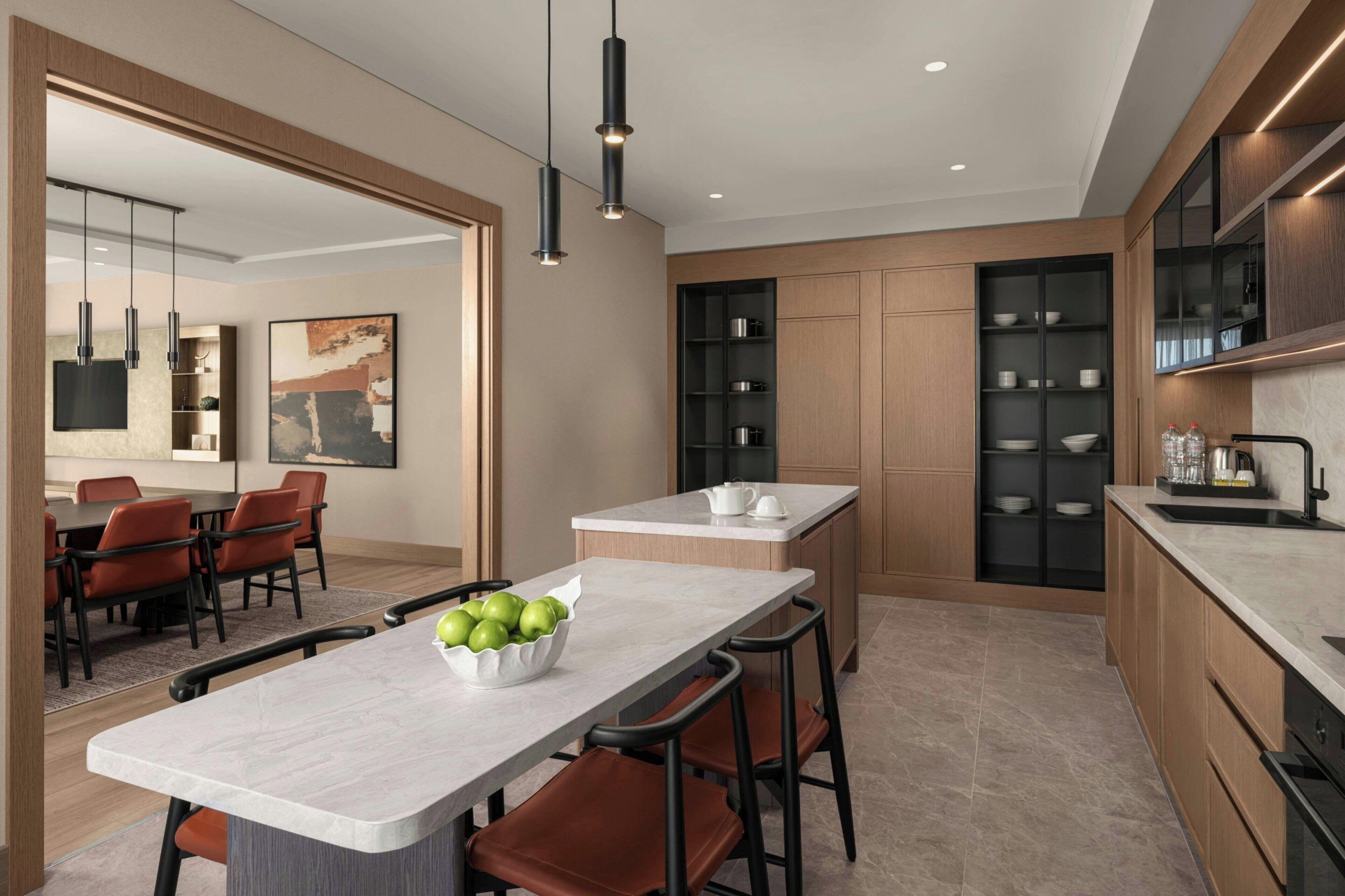A modern kitchen with a marble countertop, a bowl of green apples, and a dining area with chairs and a table.