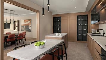 A modern kitchen with a marble countertop, a bowl of green apples, and a dining area with chairs and a table.