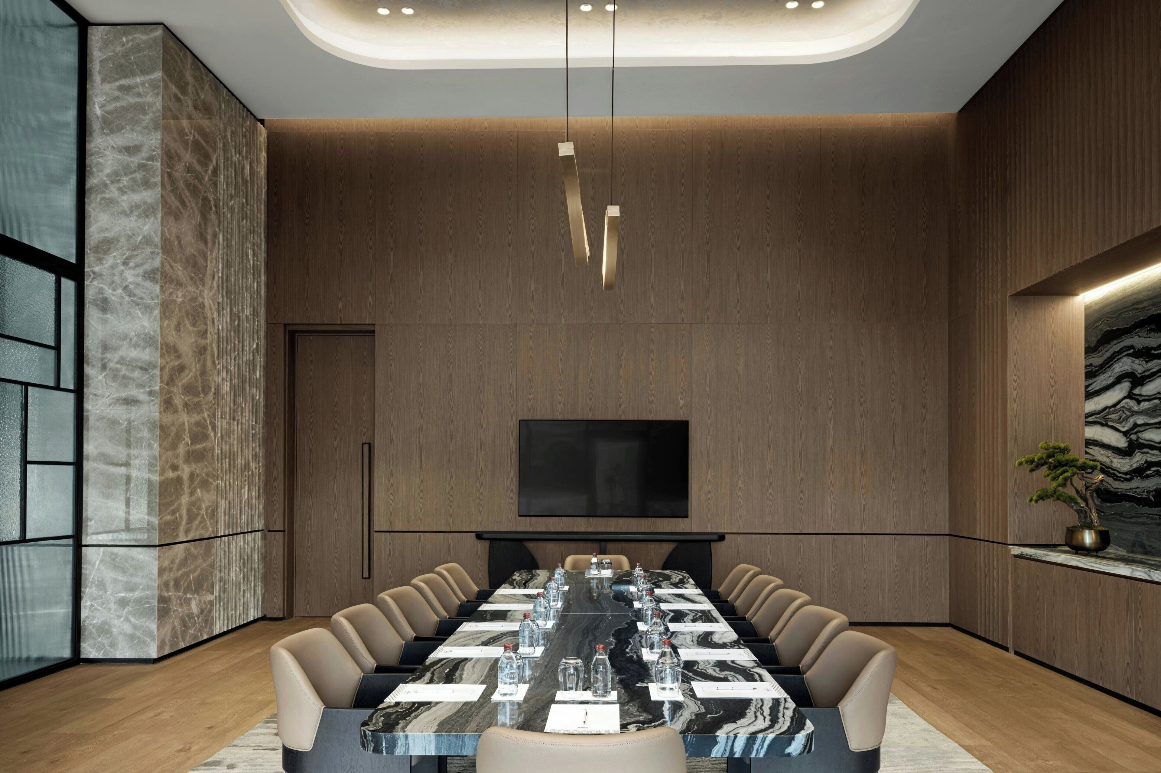 A modern conference room with a long table, comfortable chairs, a flat-screen TV, and a large potted plant.