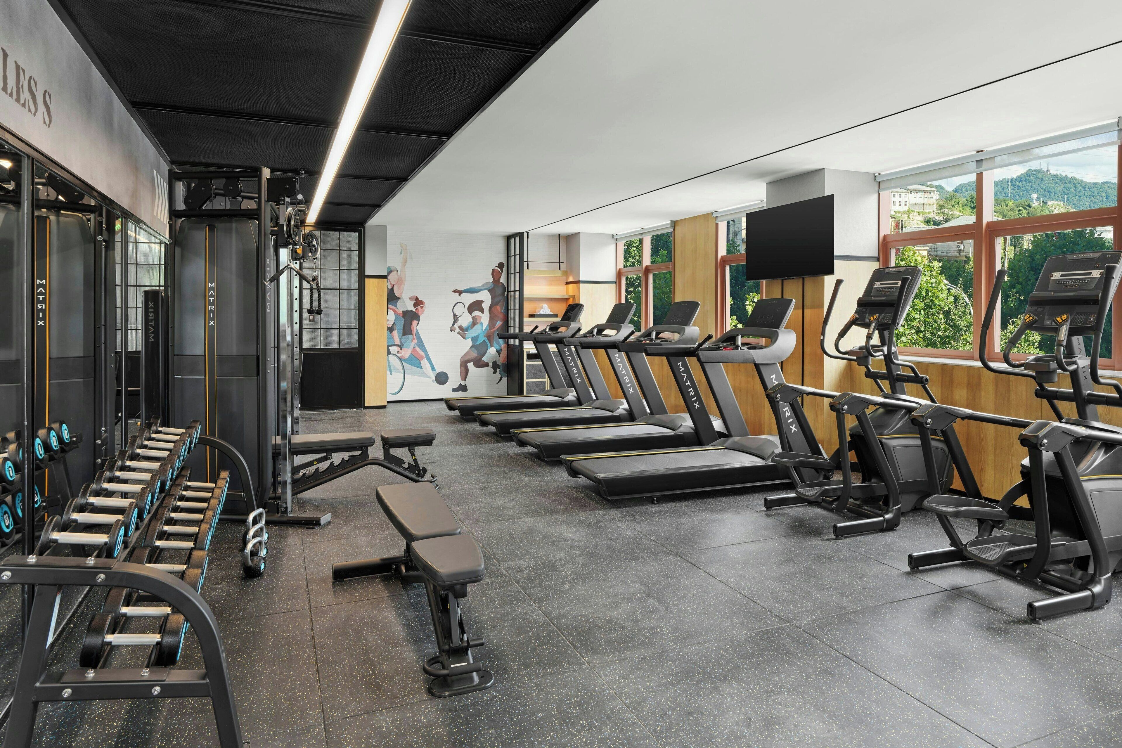 Une salle de sport équipée de tapis de course, d’appareils de musculation et d’haltères.
