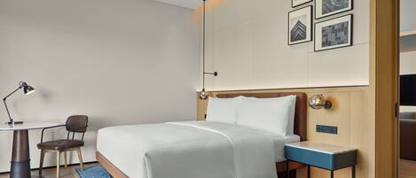 Una habitación de hotel moderna con una cama bien hecha, un escritorio con lámpara, una silla y una mesita.