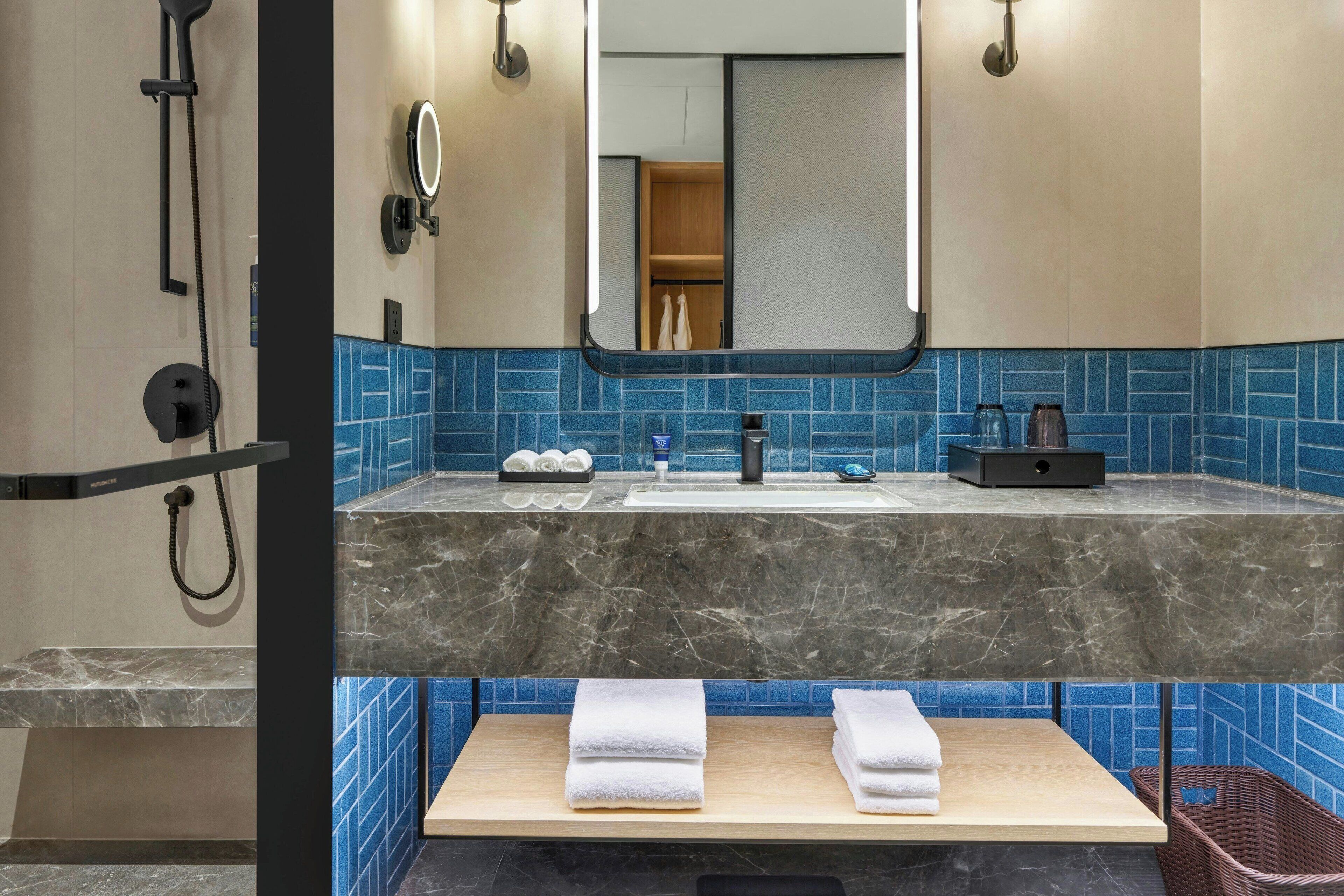 A modern bathroom with a marble countertop, a sink, a mirror, and a shower area.