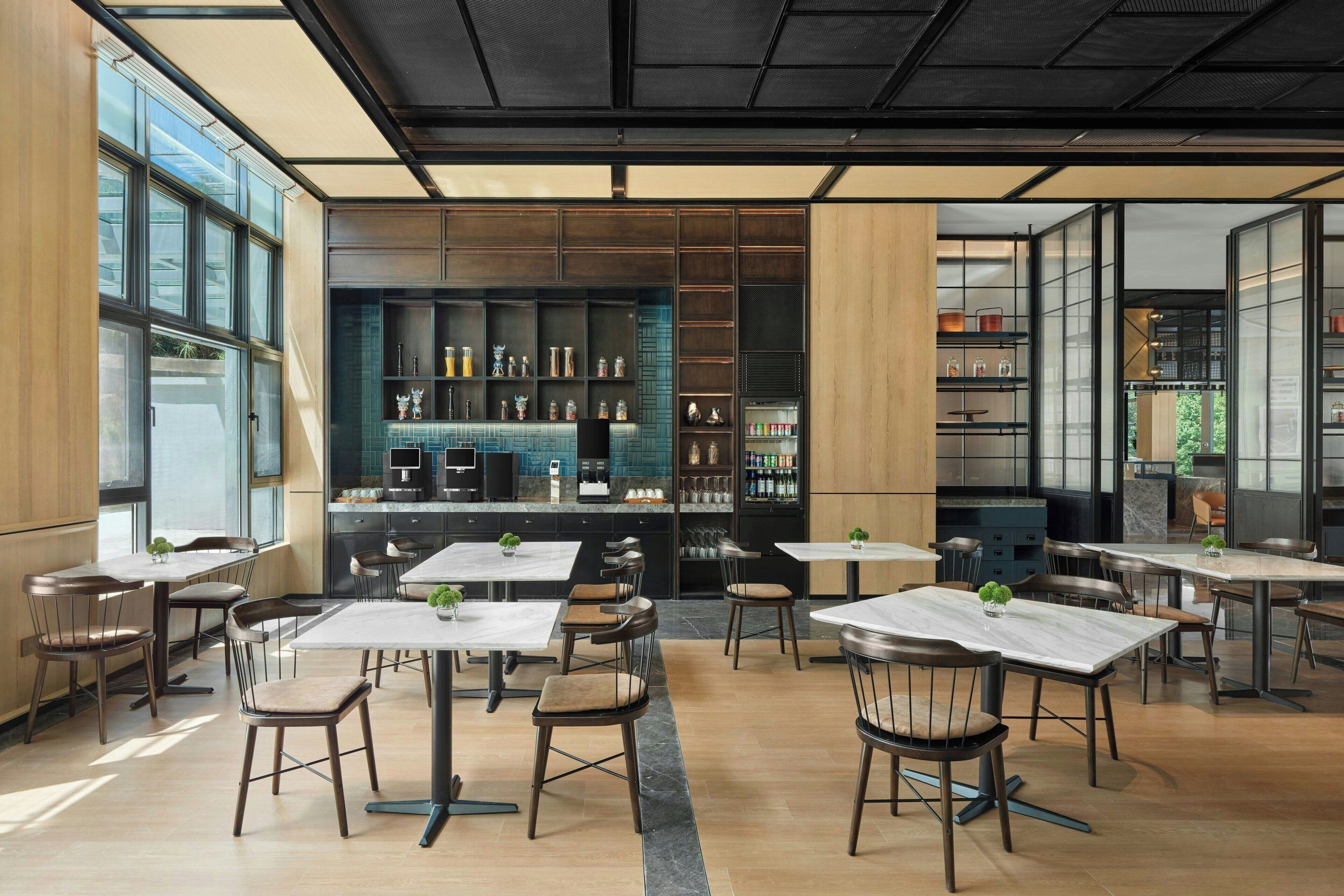 Un restaurant moderne doté de nombreuses tables et chaises, d’un bar et d’une cuisine visible à travers des cloisons en verre.