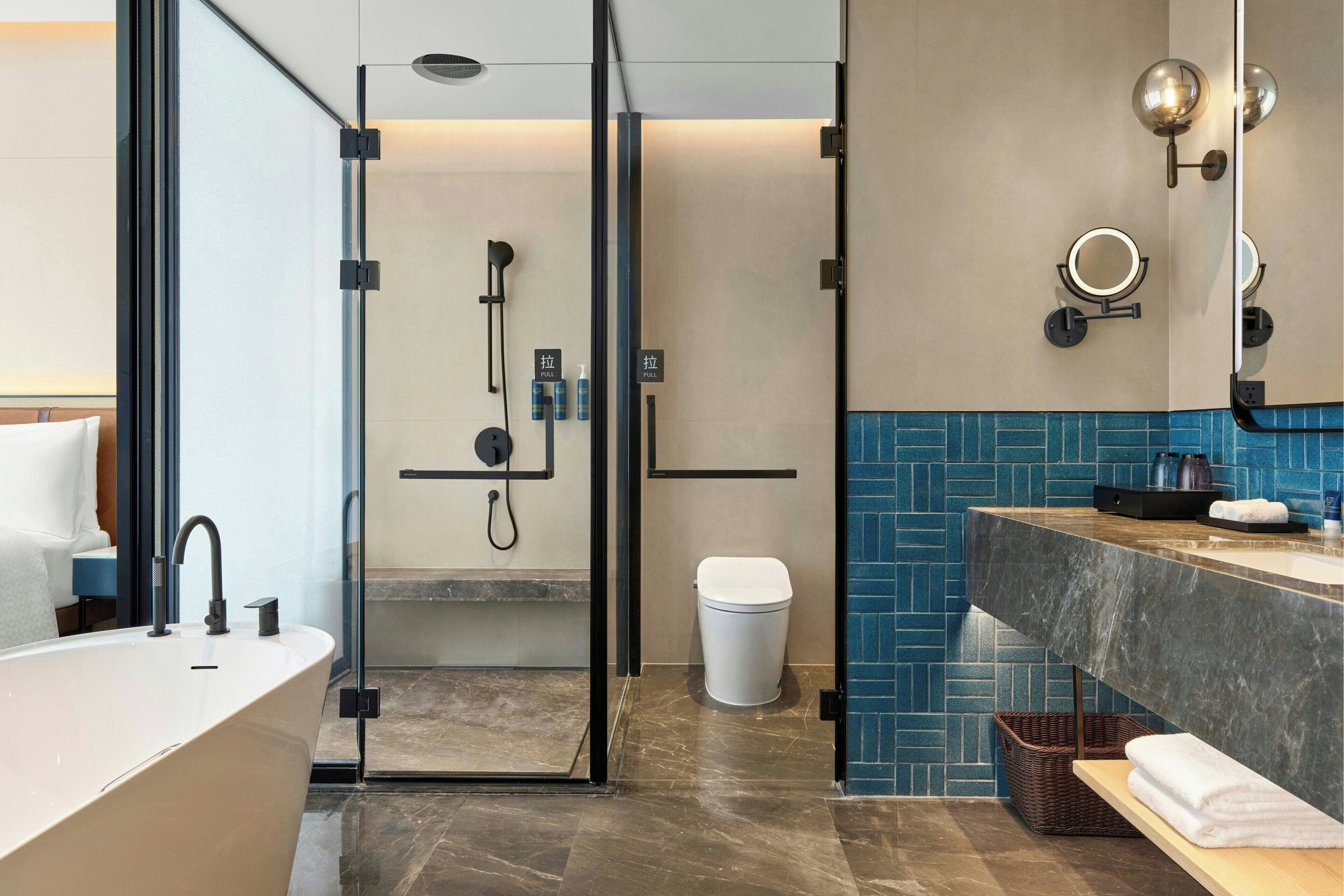 A modern bathroom with a freestanding bathtub, a glass-enclosed shower, a vanity with a marble countertop, and a blue-tiled backsplash.