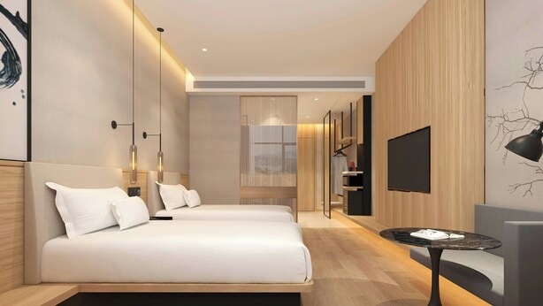 Une chambre d’hôtel moderne, dotée de deux lits, d’un téléviseur à écran plat, d’une petite table ronde et d’une grande fenêtre.