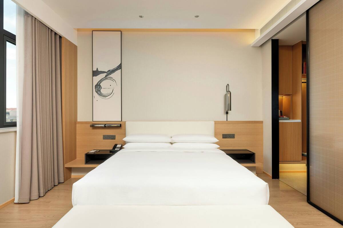 Ein modernes Hotelzimmer mit einem großen Bett, Nachttischen, einem Wandkunstwerk und einer Schiebetür zu einem Badezimmer.