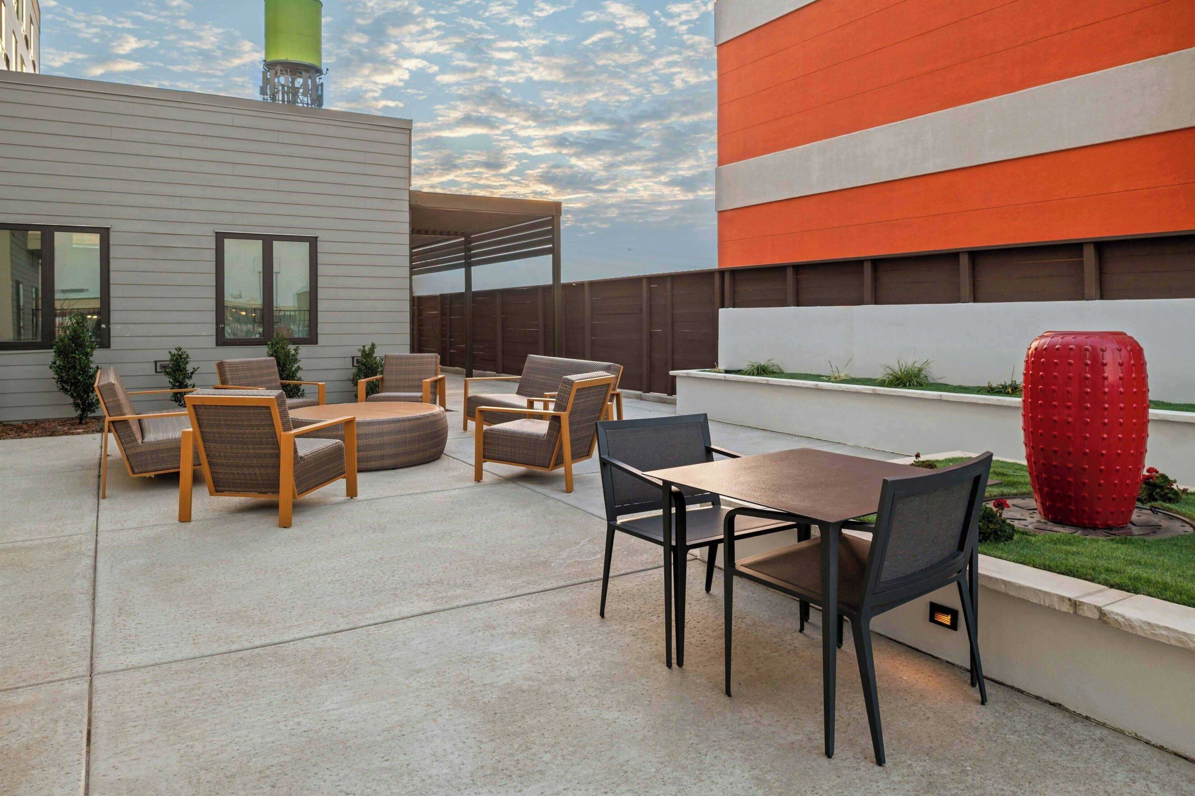 Un patio al aire libre con una mesa, sillas, una escultura decorativa roja y un edificio moderno en el fondo.