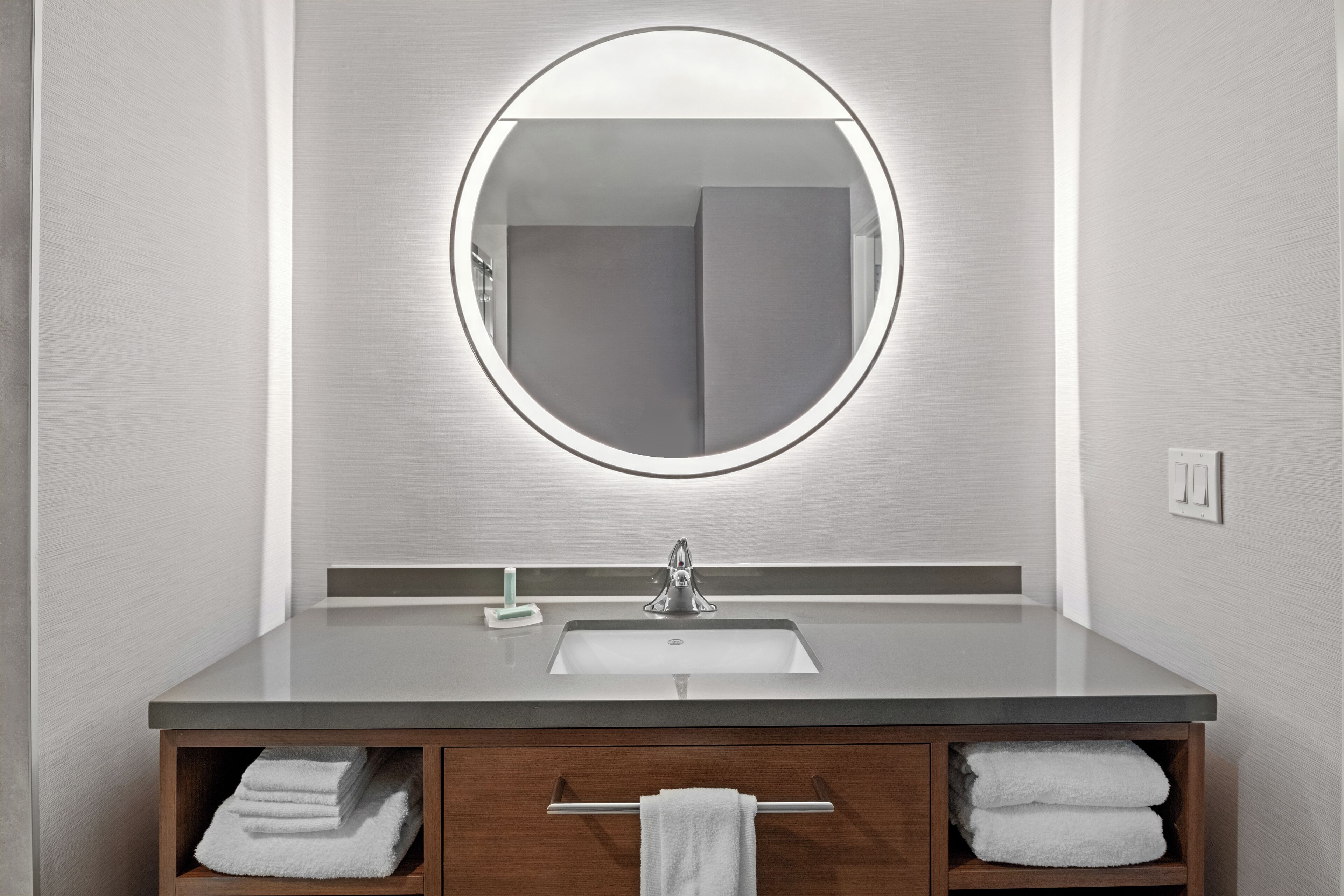 Un baño moderno con un espejo redondo, un lavabo y armarios de madera.