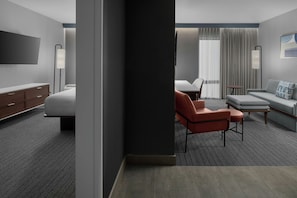 Una habitación de hotel con cama, escritorio, silla, sofá, televisor y lámpara.