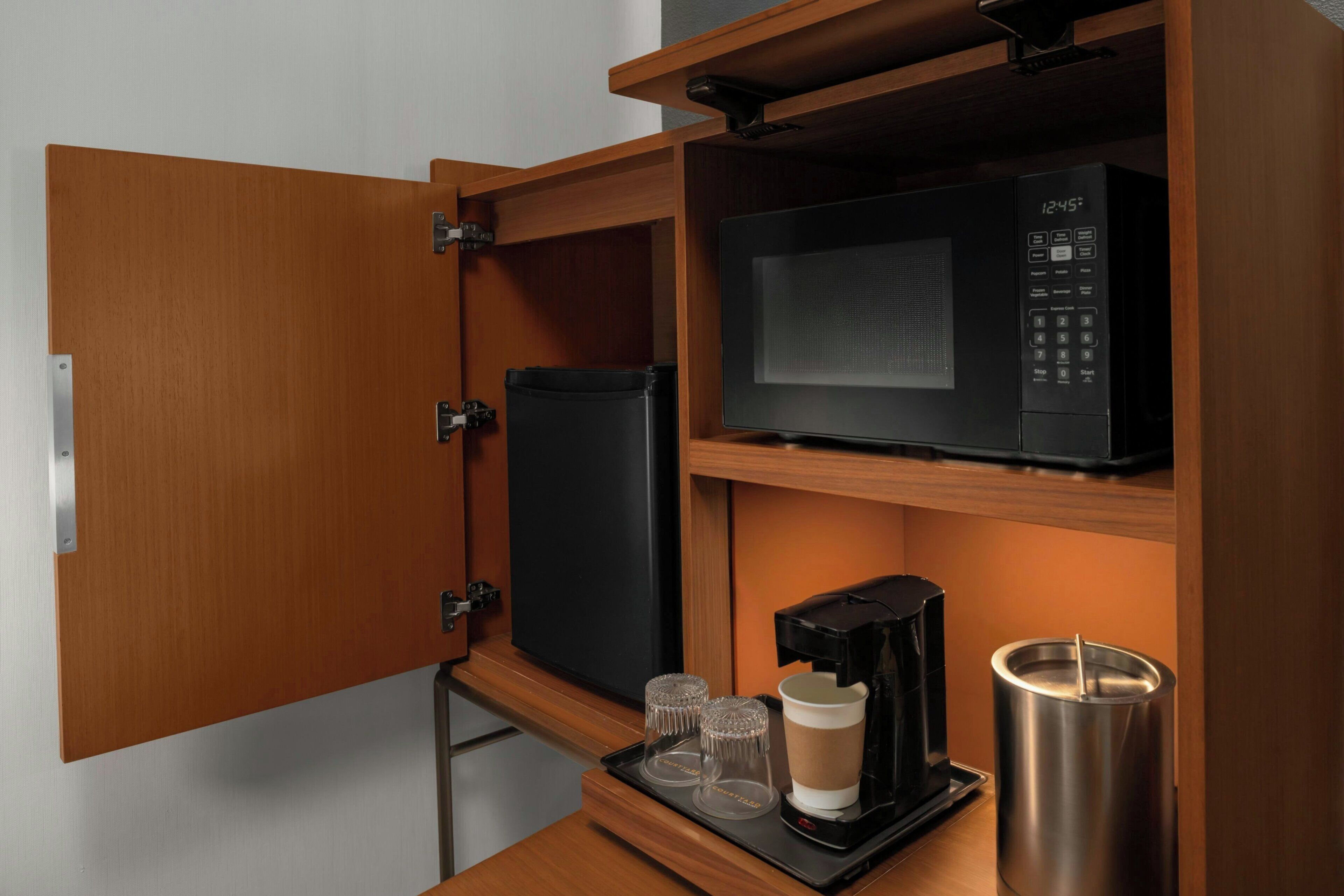 Una kitchenette compacta con microondas, cafetera y recipiente de acero inoxidable.