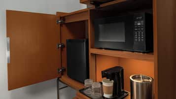 Una kitchenette compacta con microondas, cafetera y recipiente de acero inoxidable.