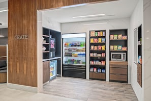 Una kitchenette moderna con refrigerador, microondas y estantes llenos de botanas y bebidas.