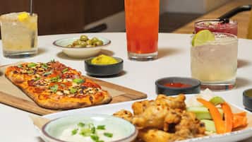 Una mesa con una variedad de comida y bebidas, incluyendo pizza, alitas de pollo y cócteles.