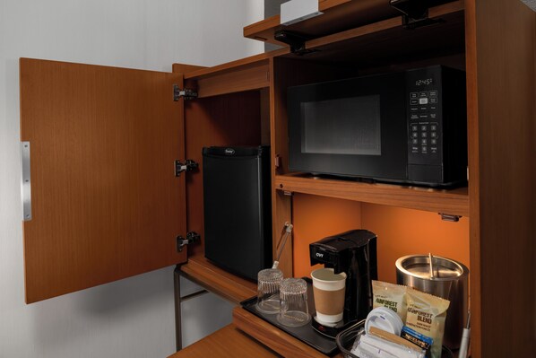 Una kitchenette compacta con microondas, cafetera y refrigerador.