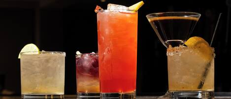 Four glasses of different beverages on a reflective surface.