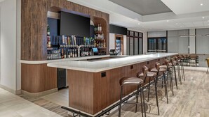Zona de bar moderna con una barra larga, varios taburetes y una gran variedad de botellas y vasos.