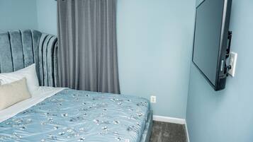 Quarto com cama, cortinas cinzas, televisão montada e parede azul claro.