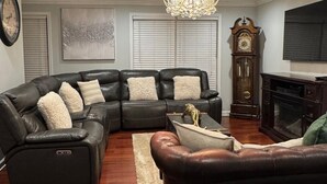 A living room with a sectional sofa, a fireplace, a chandelier, and a clock.
