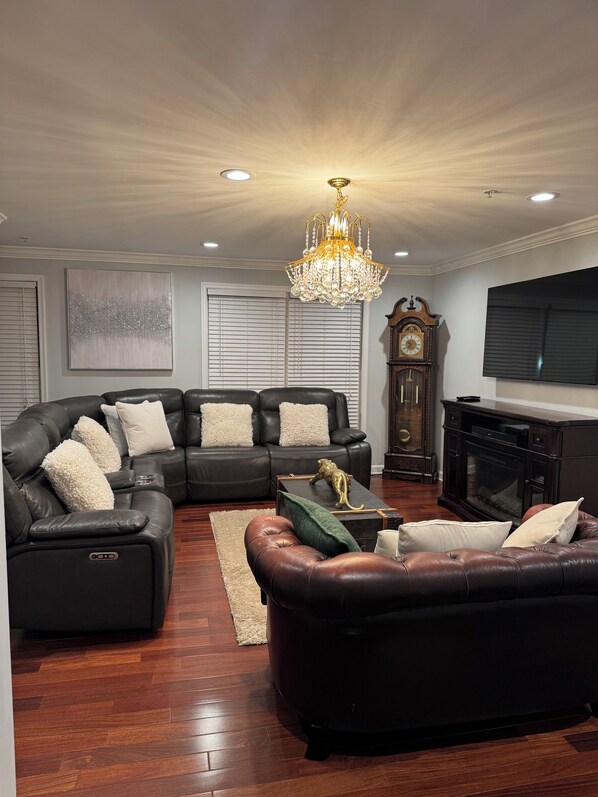 A living room with a sectional sofa, a fireplace, a chandelier, and a large television.