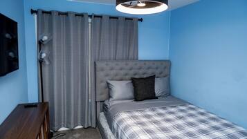 A bedroom with a bed, curtains, a lamp, and a TV on the wall.