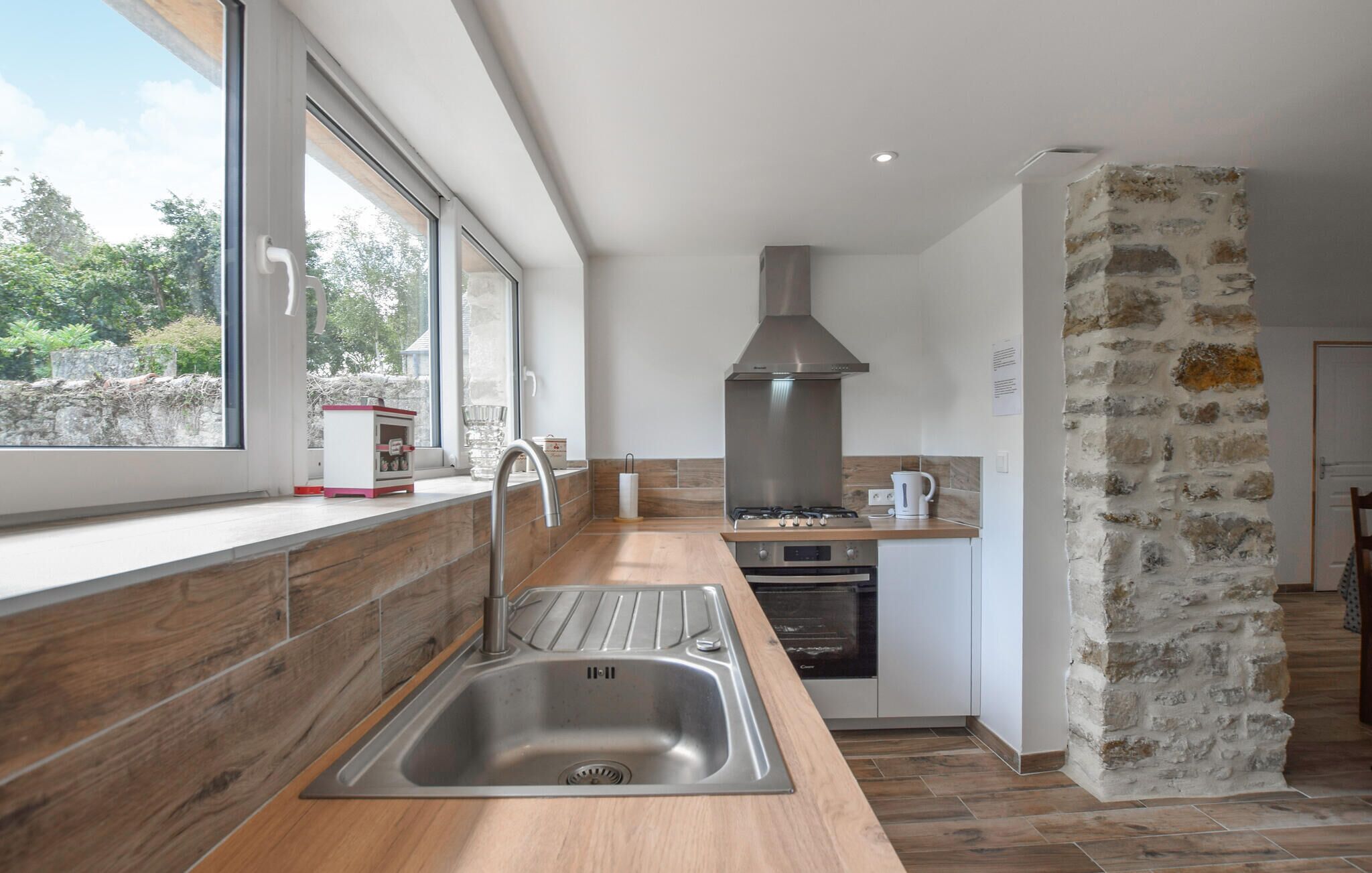 A modern kitchen with a stainless steel sink, wooden countertop, and a stone wall.