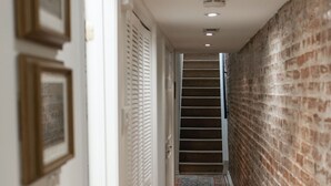 Un pasillo con suelo de madera, pared de ladrillo y un extintor de incendios colgado en la pared.