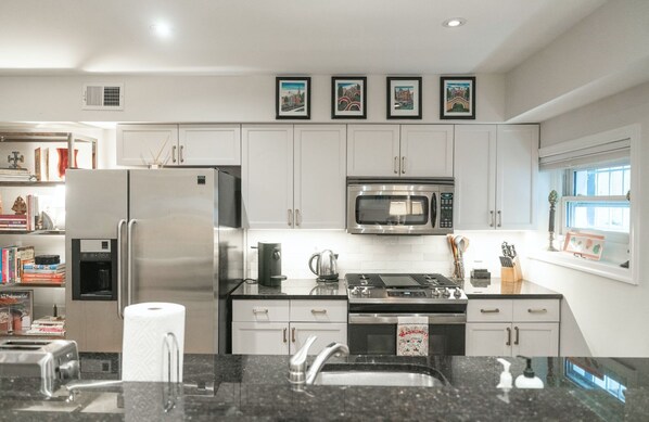 A modern kitchen with stainless steel appliances, white cabinetry, and a granite countertop. - Five star luxury in the heart of historic DuPont Circle in DC (Washington)