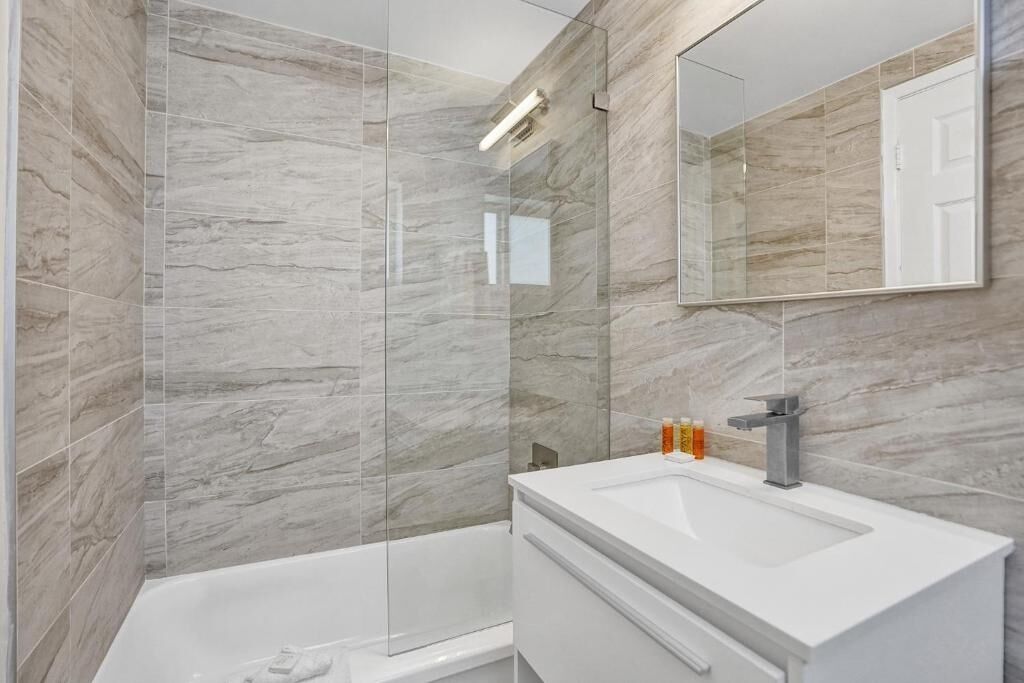 A modern bathroom with a glass-enclosed shower, a white sink, and a large mirror.