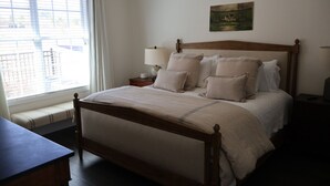 Ein ordentlich bezogenes Bett mit Holzrahmen, ein Nachttisch mit Lampe und ein Fenster mit Vorhängen.