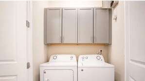 Ein Waschraum mit zwei weißen Waschmaschinen und grauen Schränken darüber.