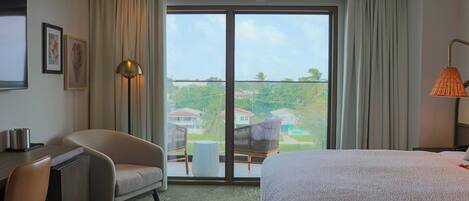 Habitación de hotel con cama, escritorio, silla, lámpara y vistas al exterior.