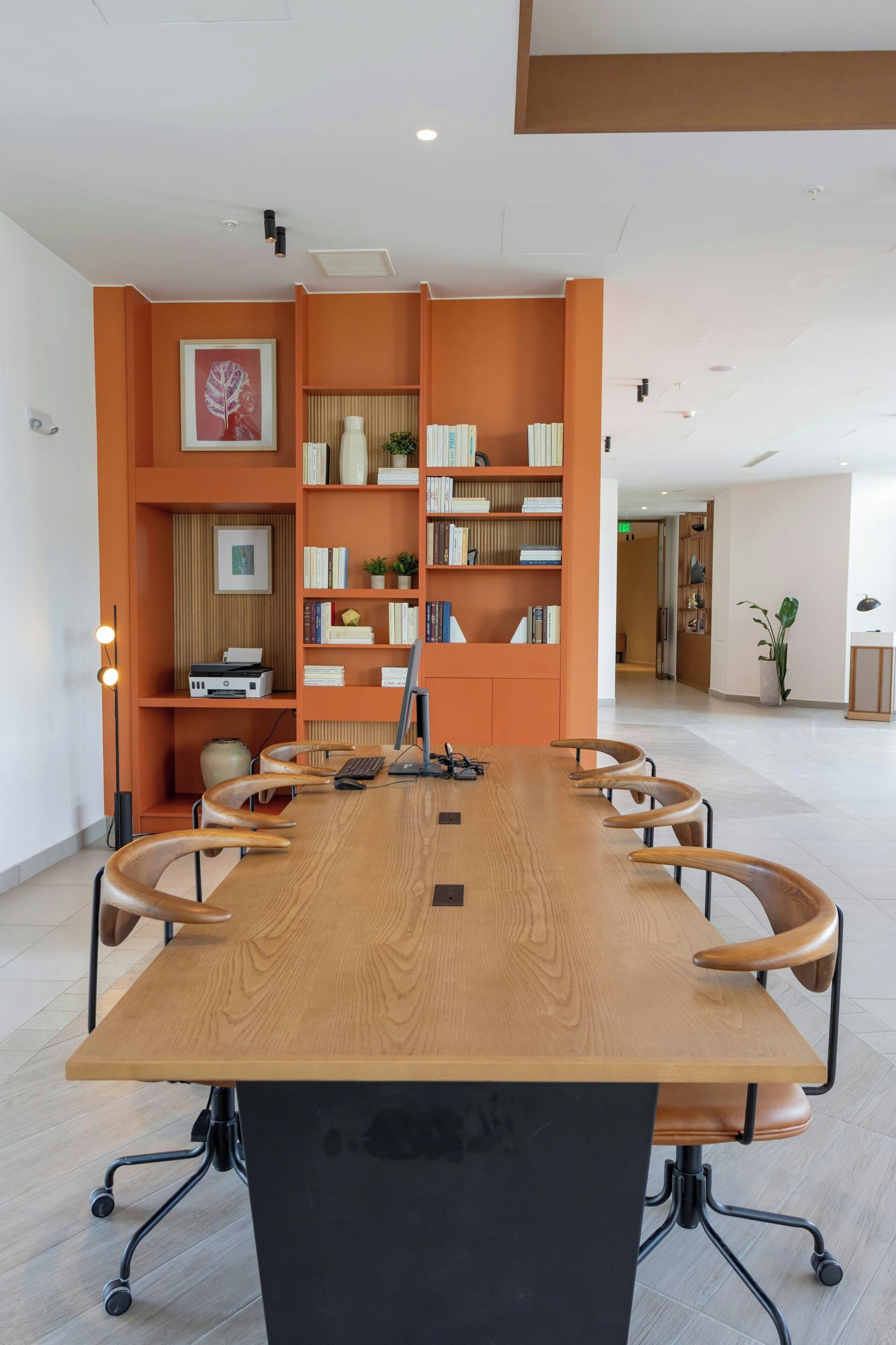 Un salón de conferencias con una larga mesa de madera, seis sillas, una computadora y estanterías con diversos objetos.