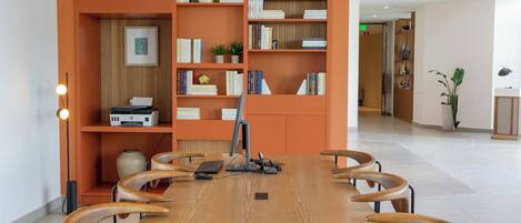 Un salón de conferencias con una larga mesa de madera, seis sillas, una computadora y estanterías con diversos objetos.
