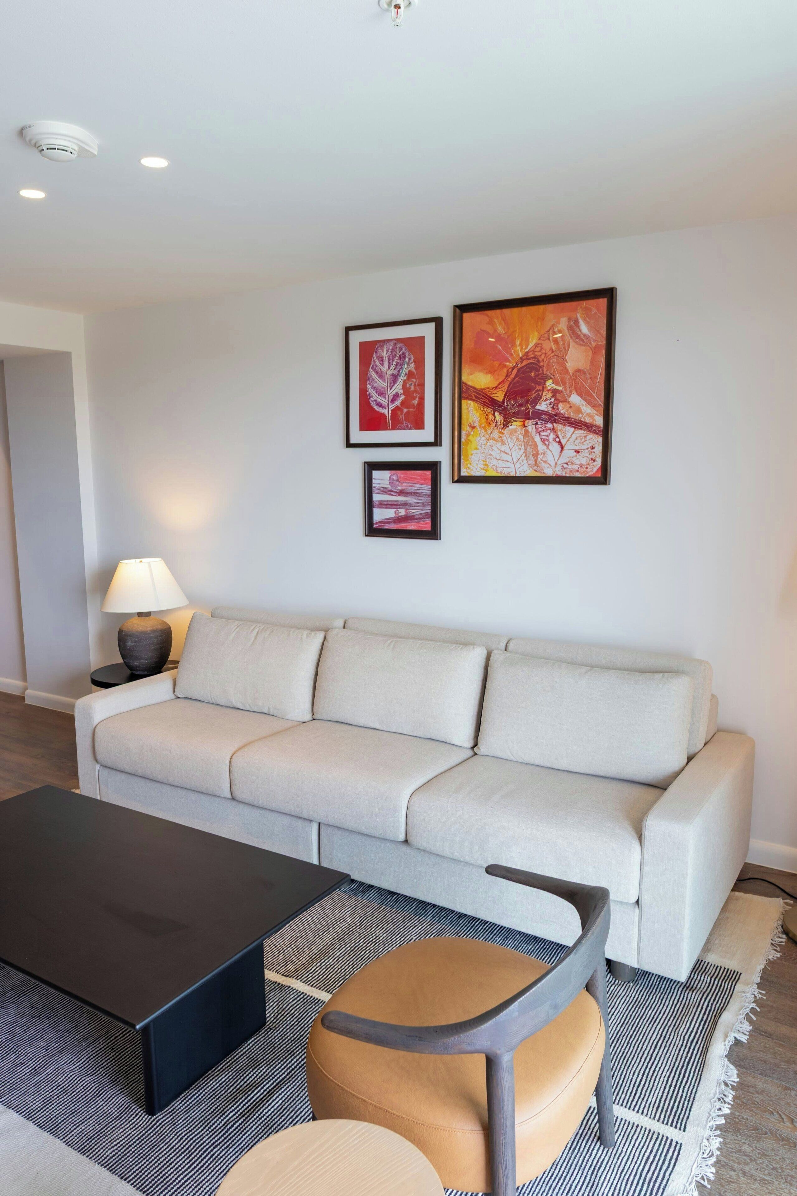 A modern living room with a sofa, a coffee table, and a lamp. There are framed artworks on the wall.
