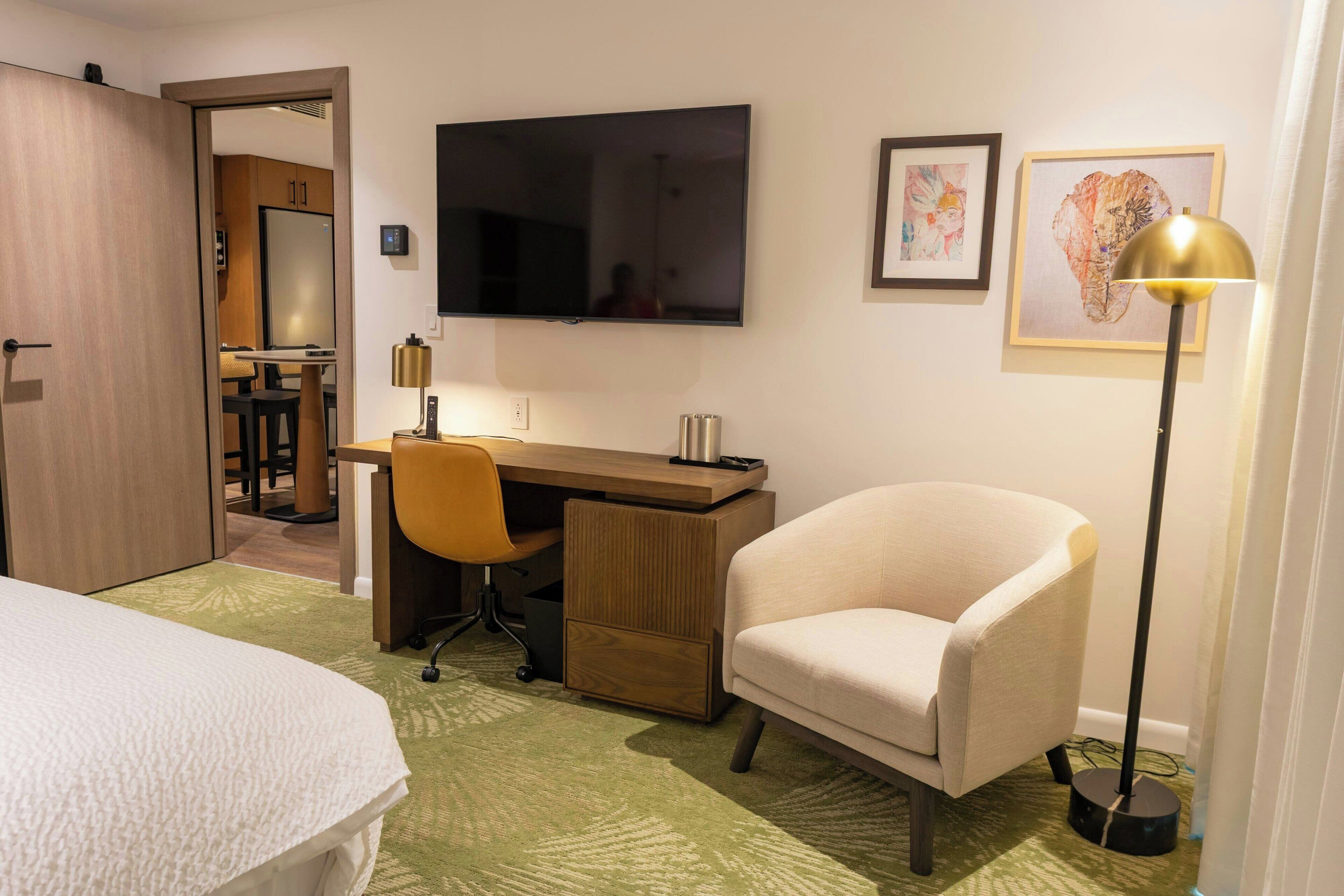 A hotel room with a bed, a desk, a chair, a TV, and a lamp.