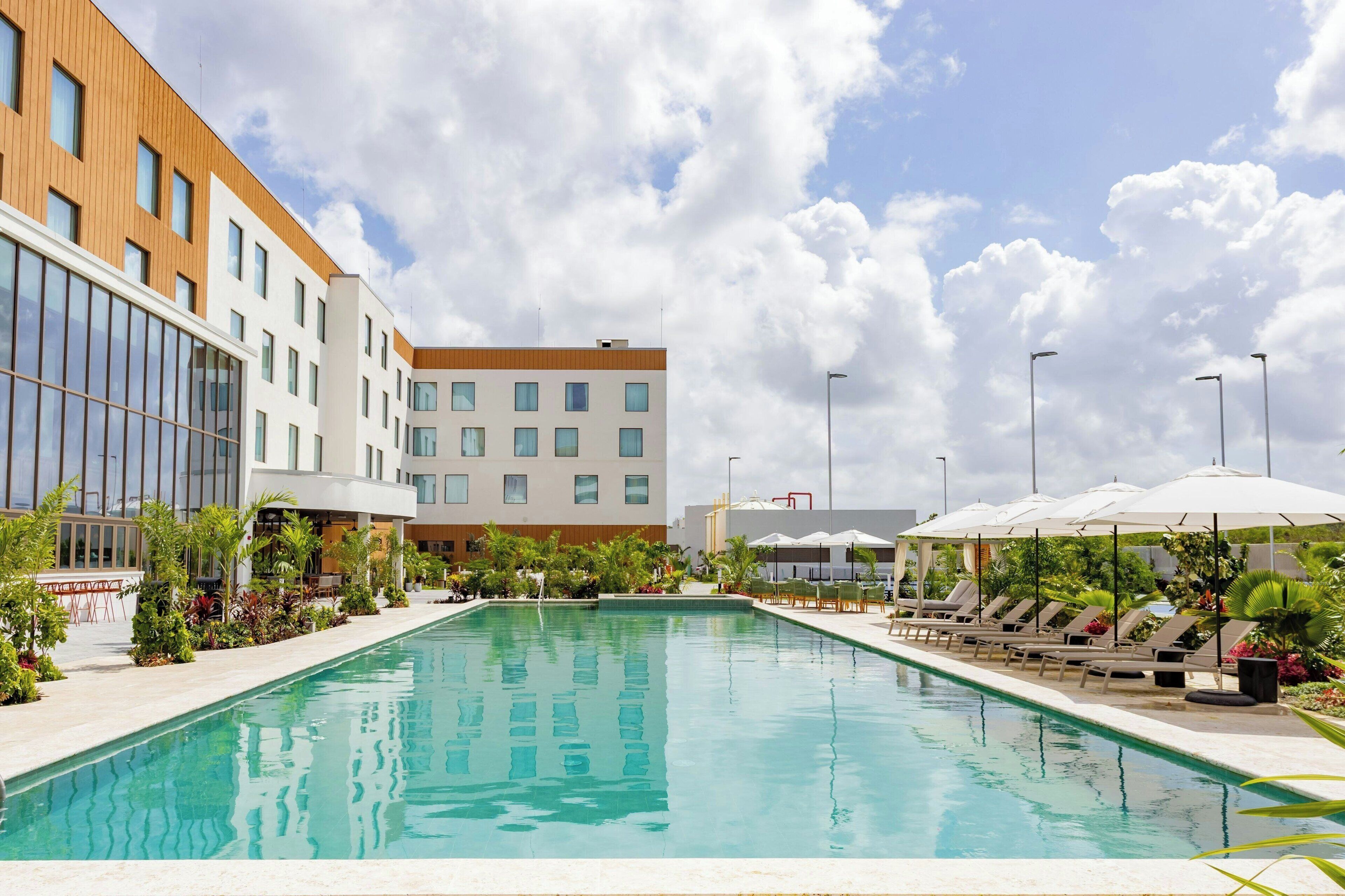 A swimming pool with lounge chairs and umbrellas, surrounded by buildings and greenery.