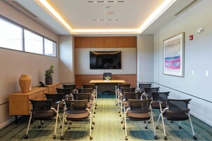 Un salón de conferencias con una mesa larga, sillas, un armario de madera, una planta y un televisor en la pared.