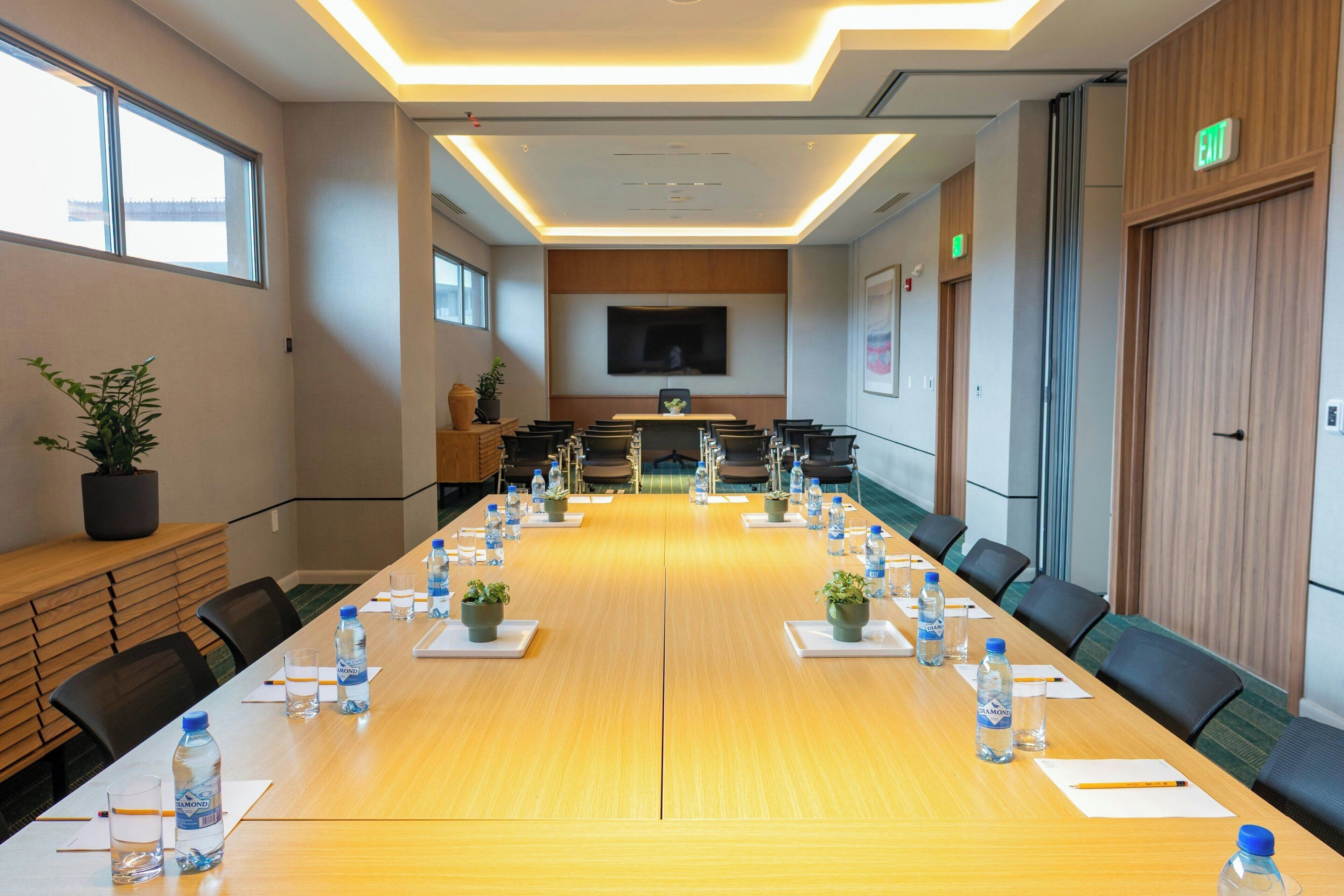 A conference room with a long table, chairs, water bottles, and potted plants.