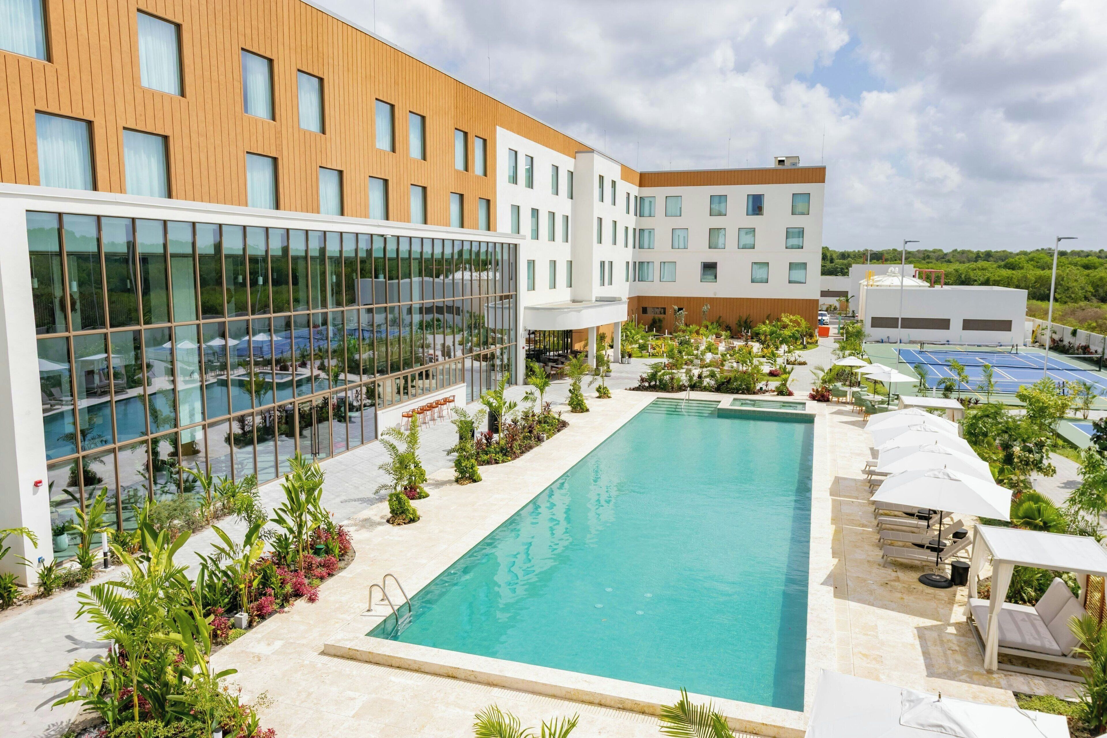 A modern hotel with a swimming pool, outdoor seating, and a glass facade.